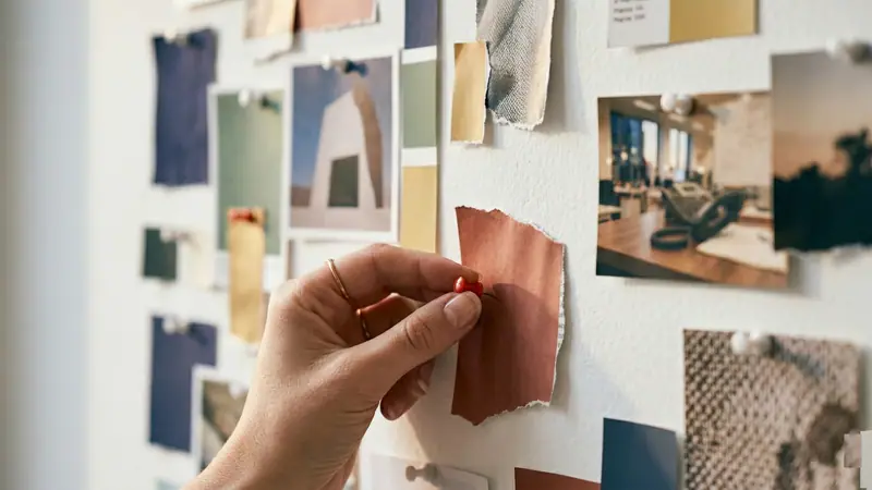 A hand pinning images to a mood board of interior design photographs